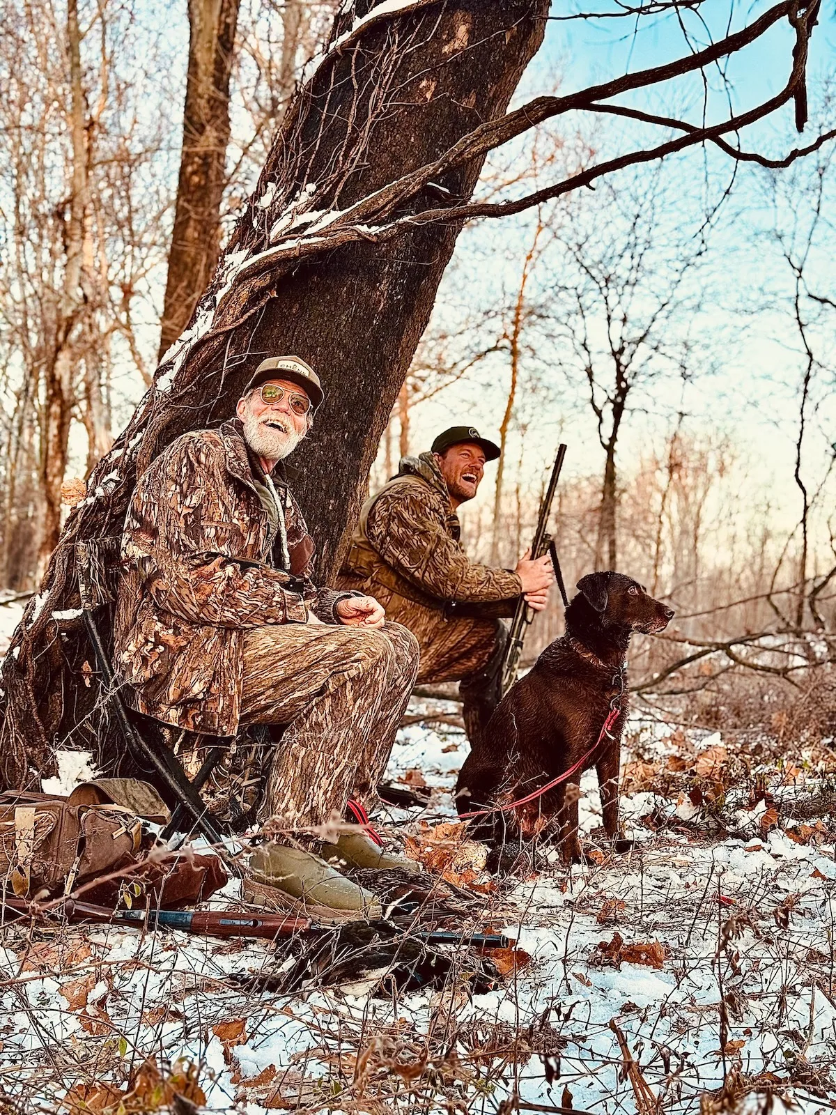 two men and a dog hunting in winter woods
