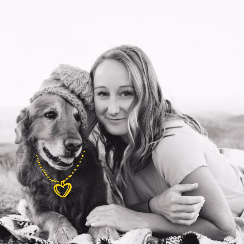 young woman and golden retriever outside on blanket looking at camera