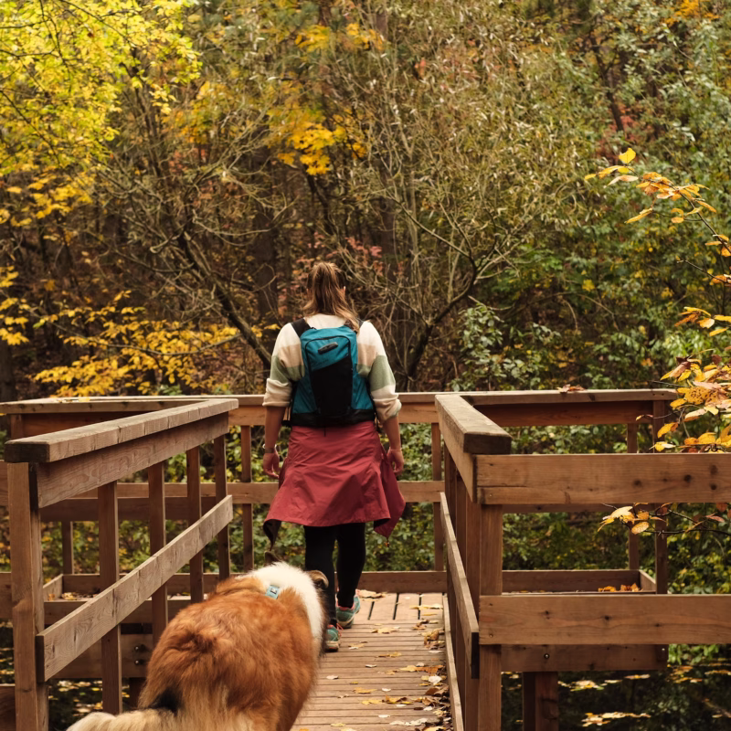 woman in warm clothing with fluffy dog walking on a boardwalk during the fall.