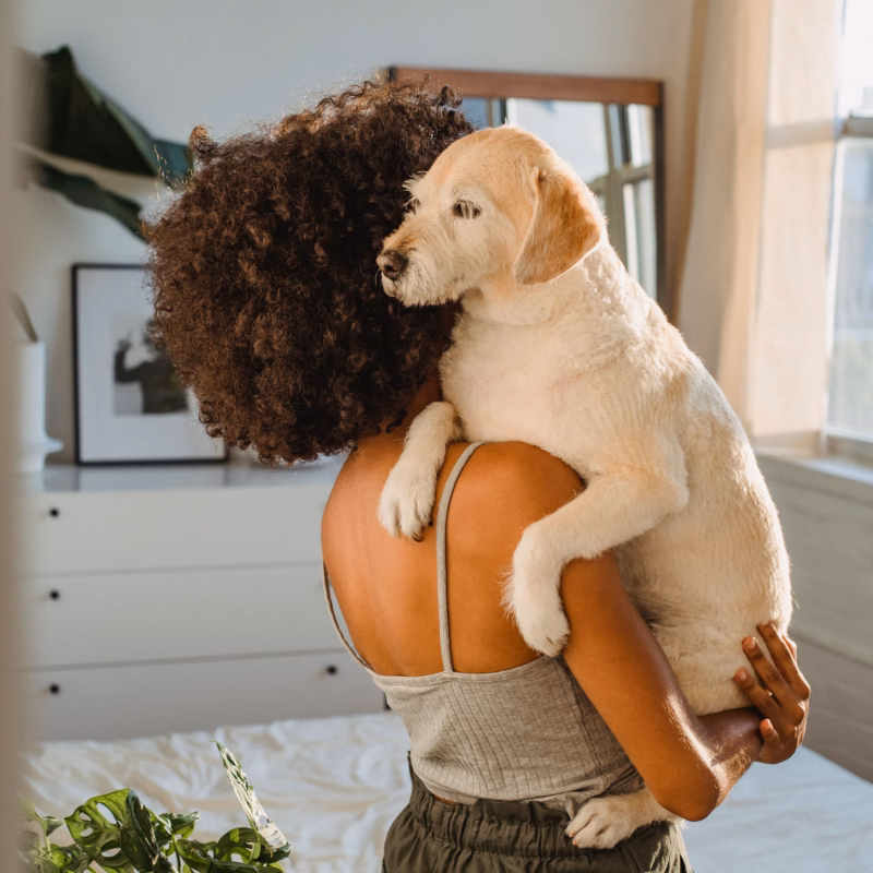 woman in grey tank top holding a white dog indoors